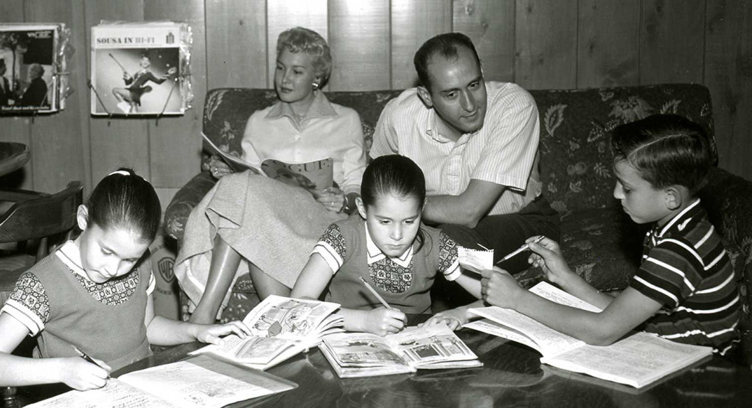 Black and White image of Henry, his wife Ginny and their three children sitting in the family room reading the newspaper and doing schoolwork.